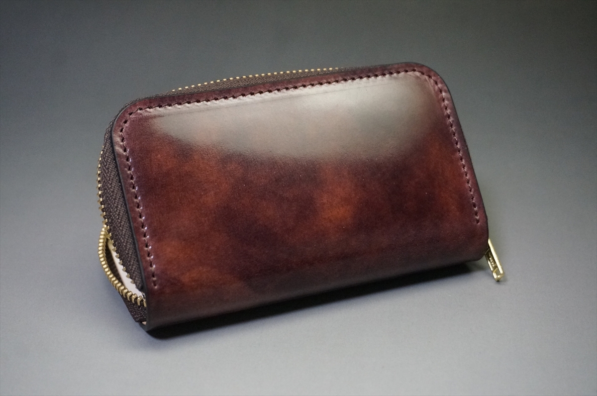 Brown leather zippered wallet with a gold zipper on a gray background, close-up view of the compact rectangular shape.