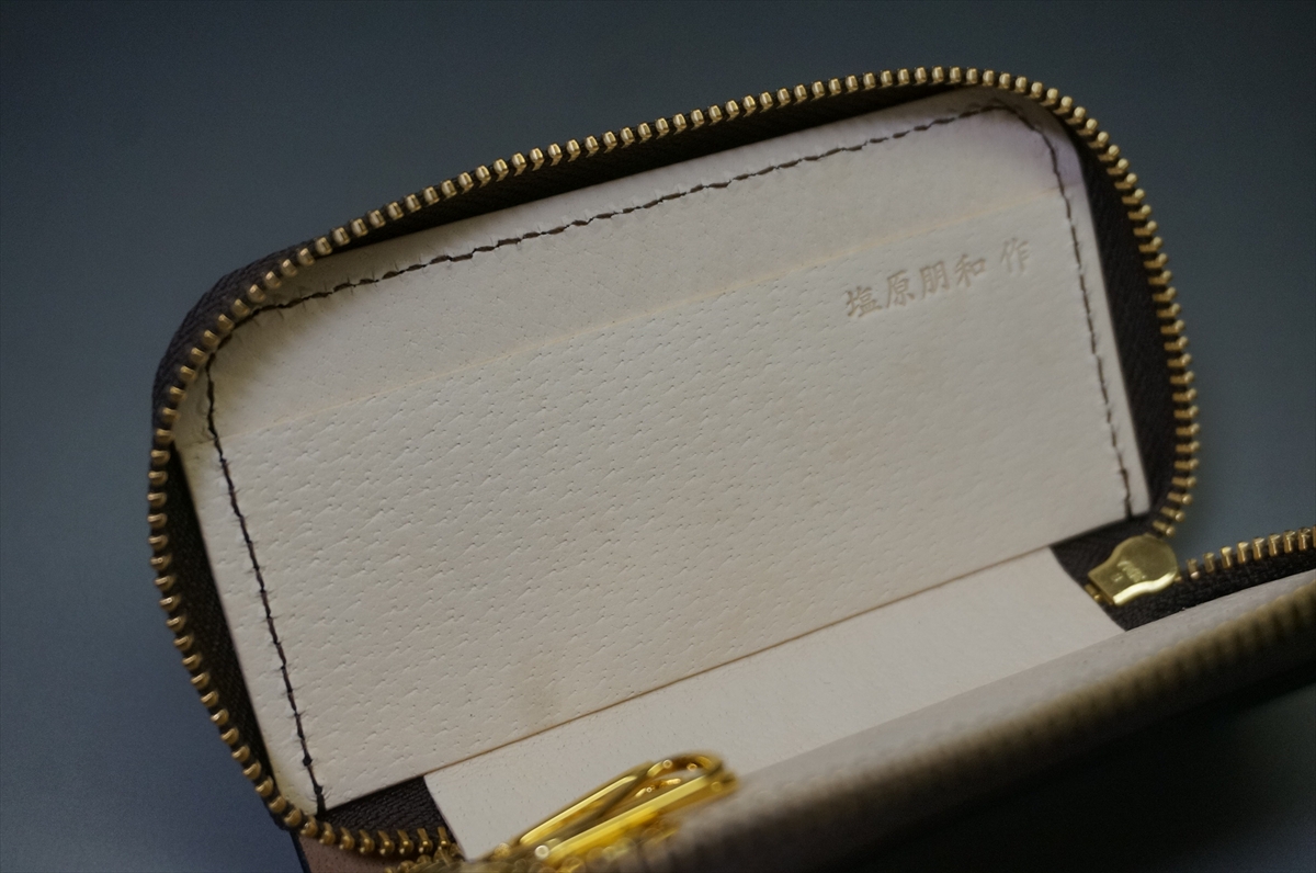 Open zippered leather pouch showing a white interior lining and a gold zipper; the inside panel has faint stamped characters (Japanese).