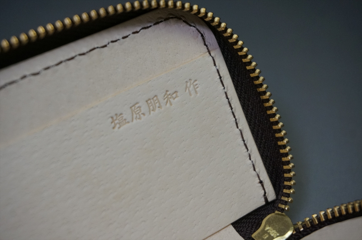 Close-up of a light leather interior with embossed Japanese characters inside a zipper pouch, showing gold teeth and dark trim.