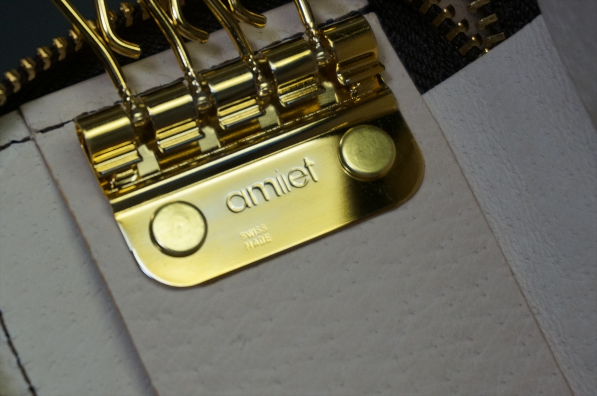 Gold-plated guitar bridge plate with 'amiet' engraving and 'SWISS MADE' on a light wood body (close-up).