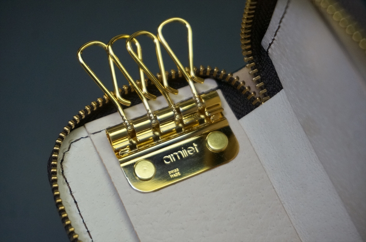 Close-up of a gold zipper on white leather, showing multiple looped zipper pulls and a branded gold plate beneath.