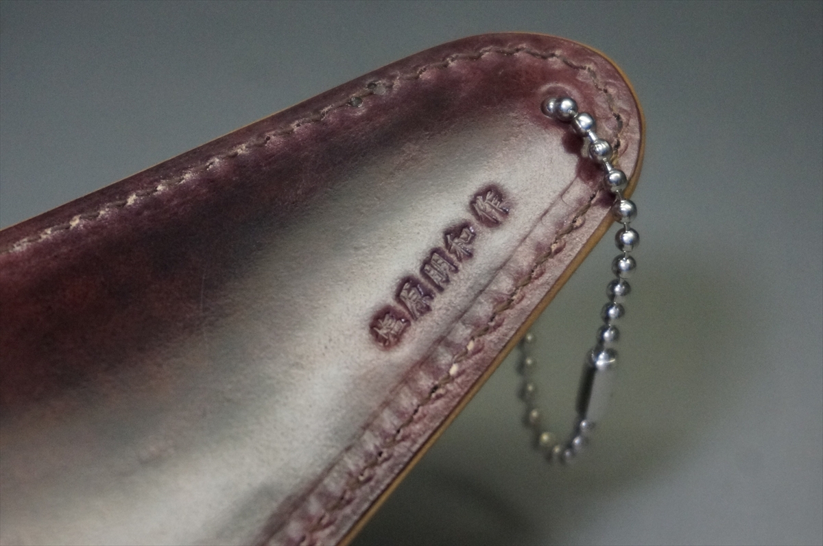Close-up of a burgundy leather case with white stitching and a silver ball-chain key ring.