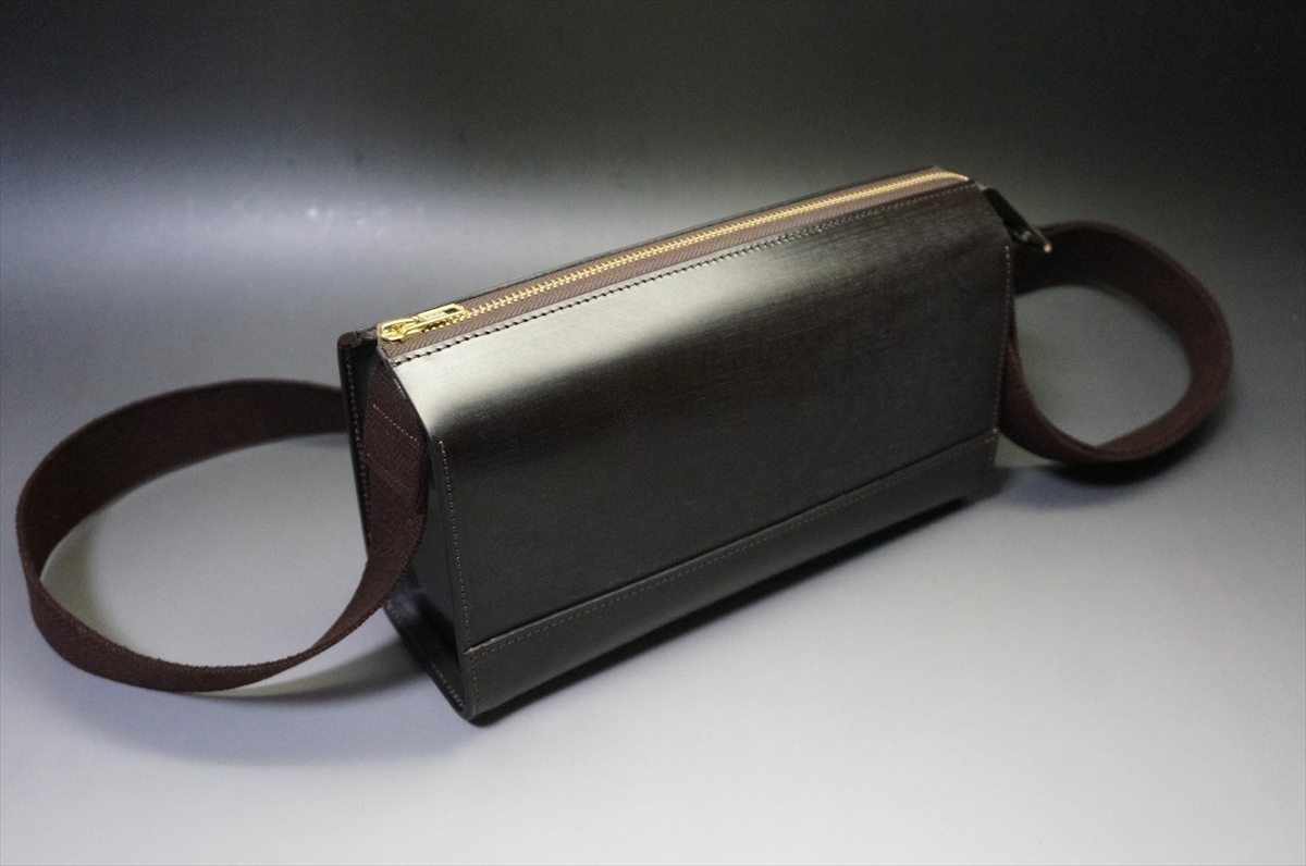 Black leather rectangular zippered pouch with brown fabric handles at each end.