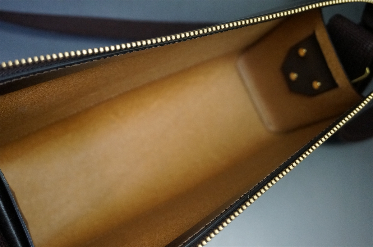 Open brown leather bag interior with light tan lining and gold zipper teeth visible along the opening.