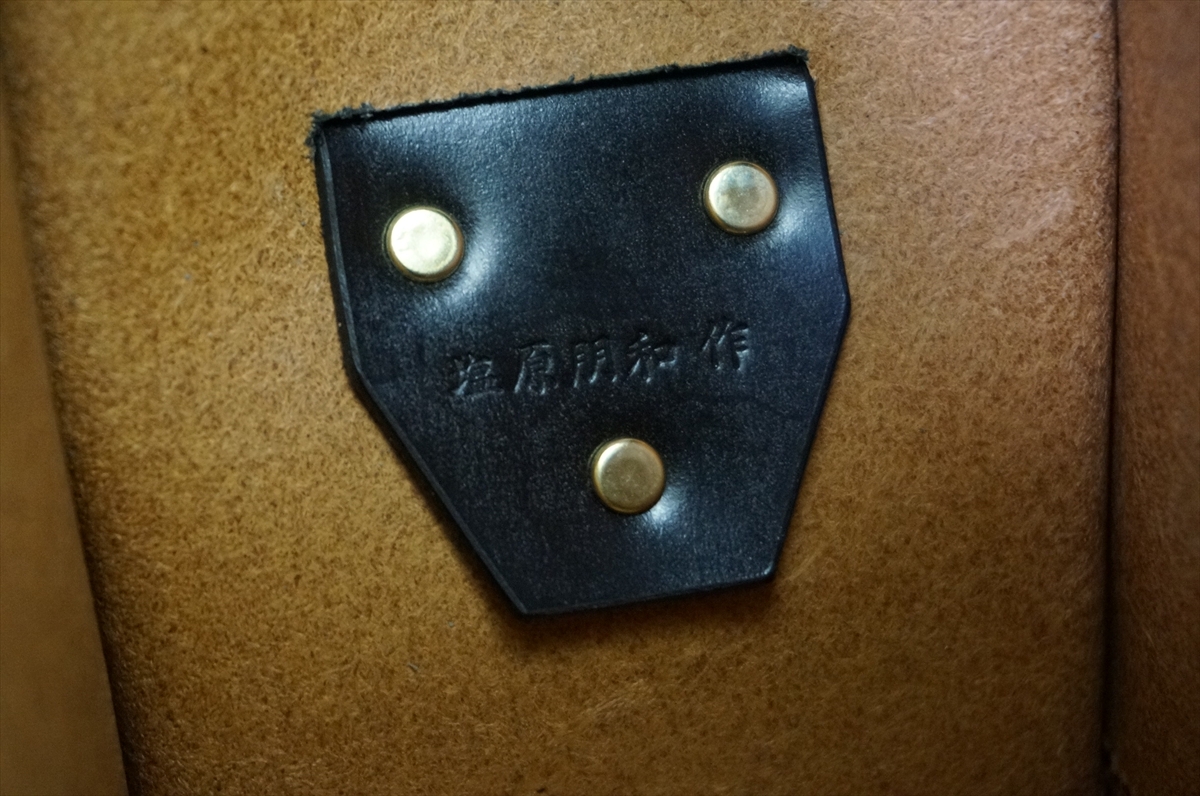 Dark blue leather patch with three brass rivets attached to brown suede material; embossed characters visible on patch.