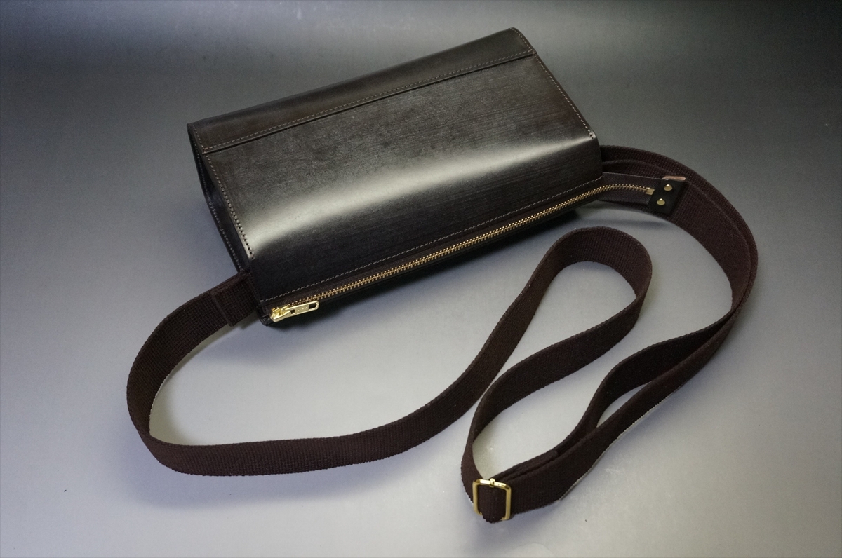 Black leather zippered wallet with a detachable brown fabric strap on a gray surface.