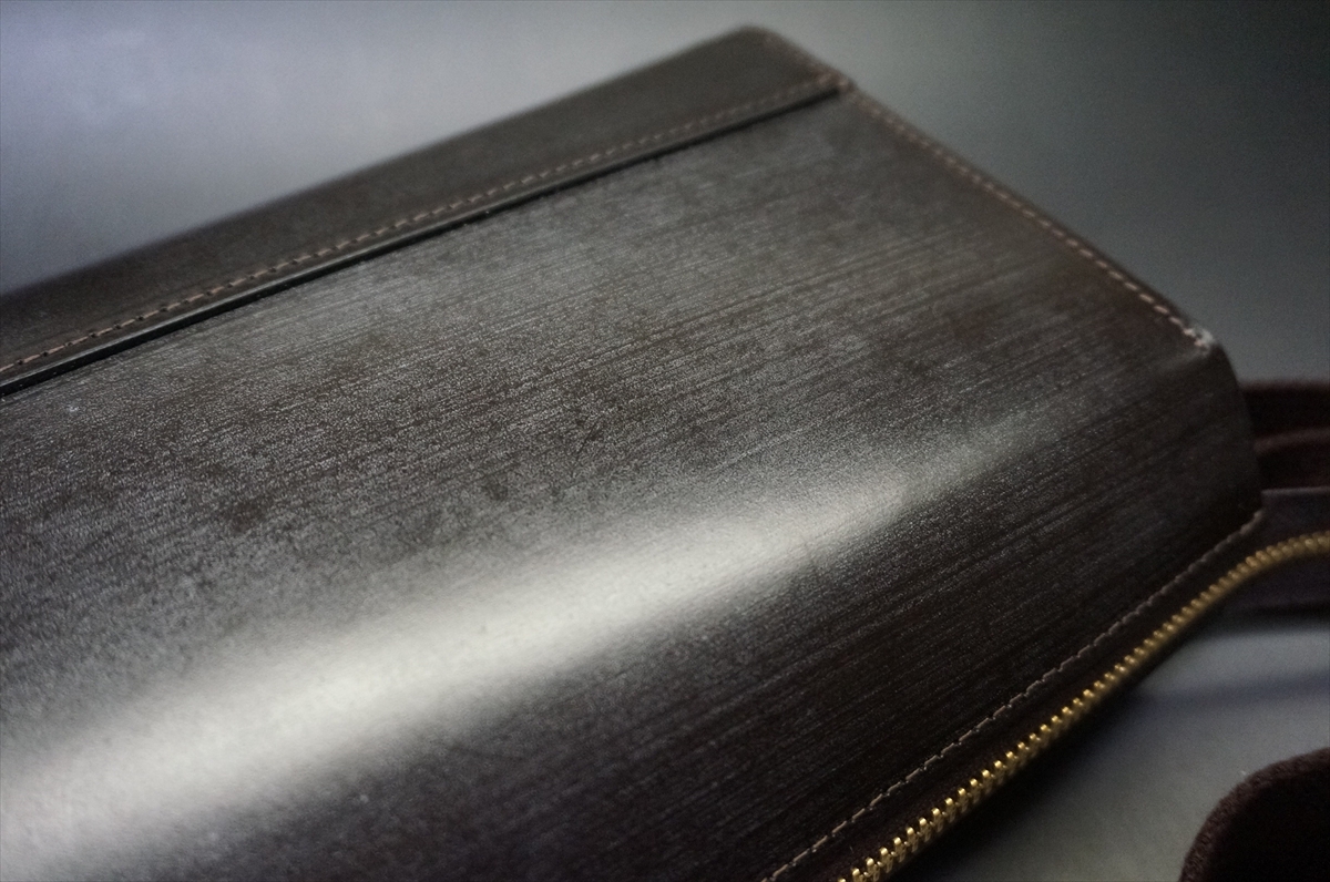 Close-up of a dark brown leather wallet with visible stitching and a gold zipper on a smooth surface.