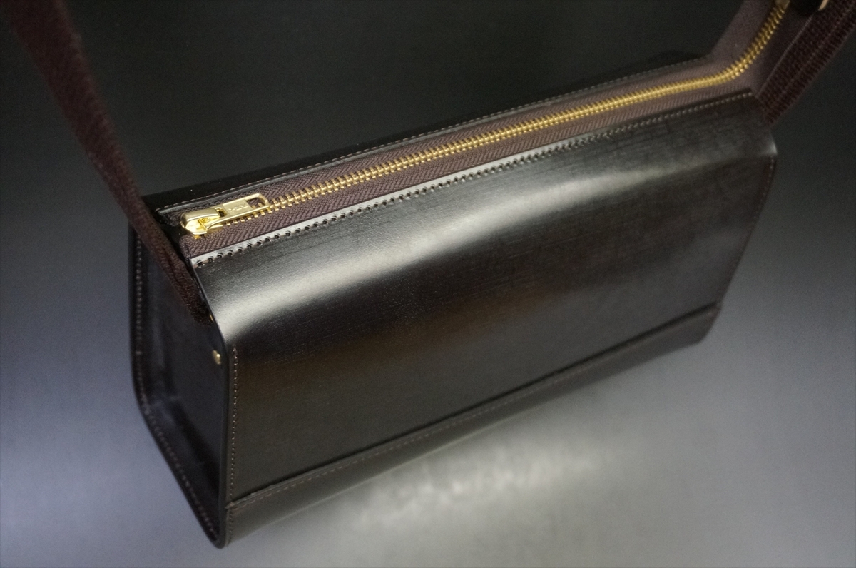 Black leather shoulder bag with a gold top zipper, photographed from an angled side view.