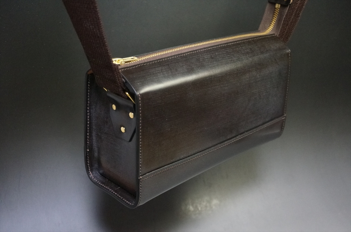 Black leather rectangular shoulder bag with a gold zipper and dark brown strap, shown from the side/angled view.