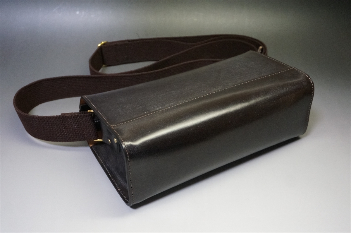 Black leather rectangular bag with a wide brown adjustable strap on a gray surface
