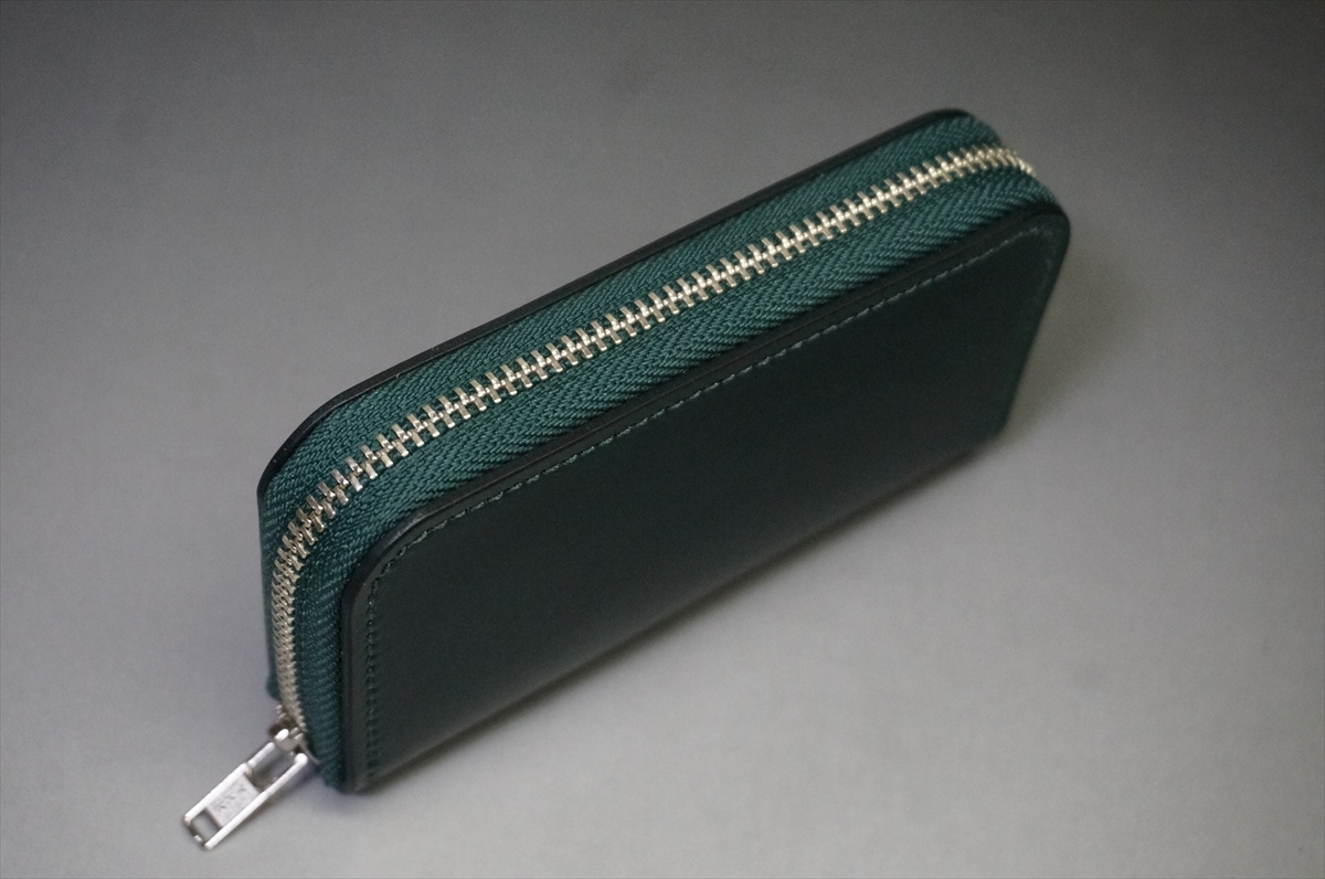 Green zippered wallet with a silver zipper, photographed on a gray surface.