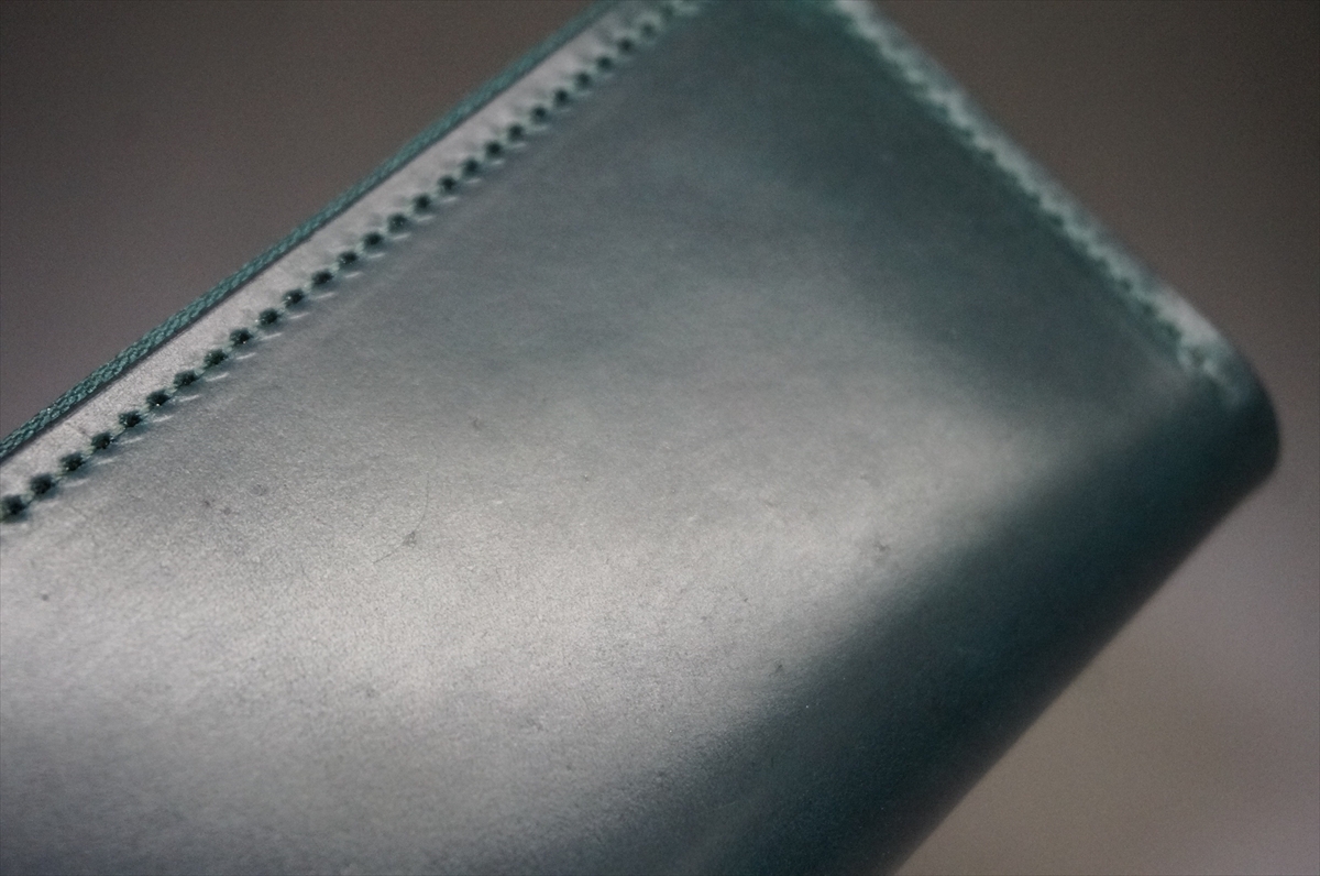 Close-up of teal leather with visible stitching along the edge, likely a wallet or bag corner.