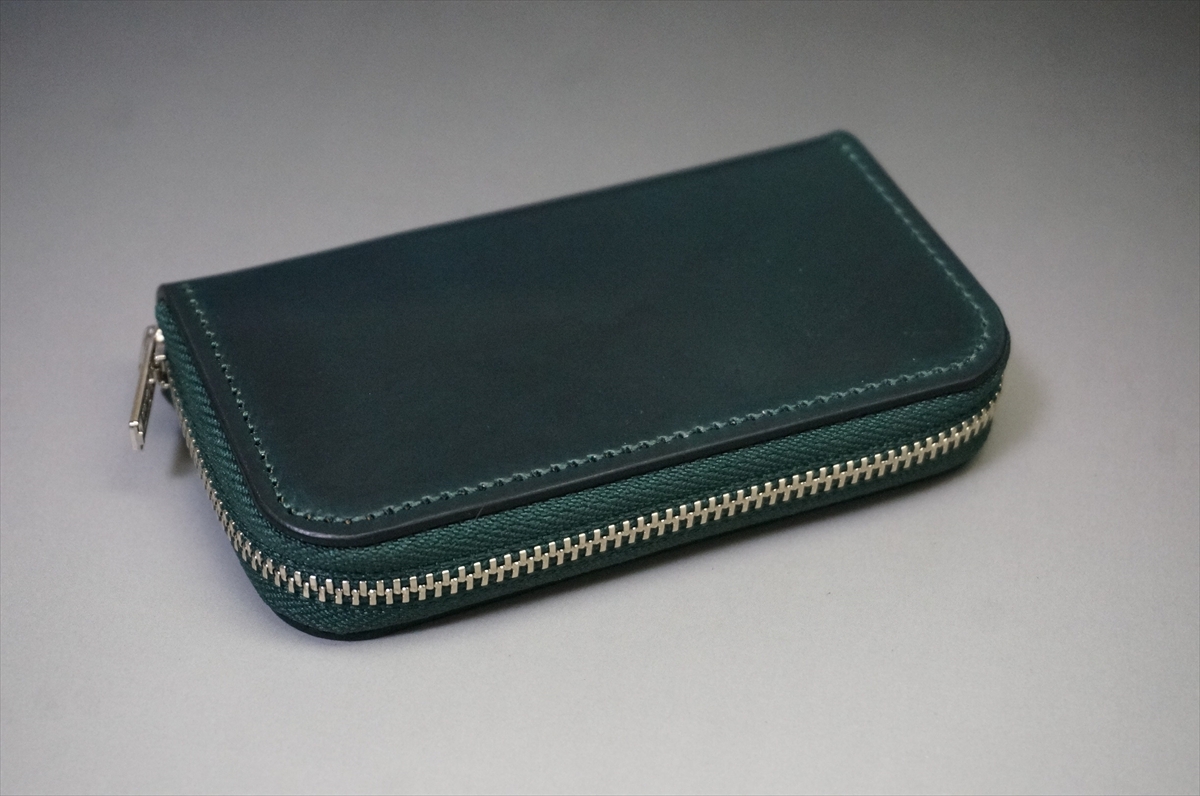Teal leather zippered wallet resting on a gray surface, zipper along the edge visible with metal teeth.