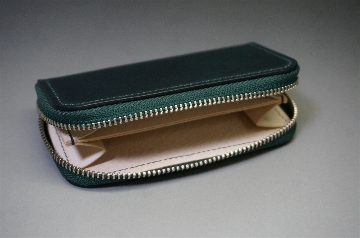 Dark green leather zip wallet opened to reveal beige interior on a gray surface
