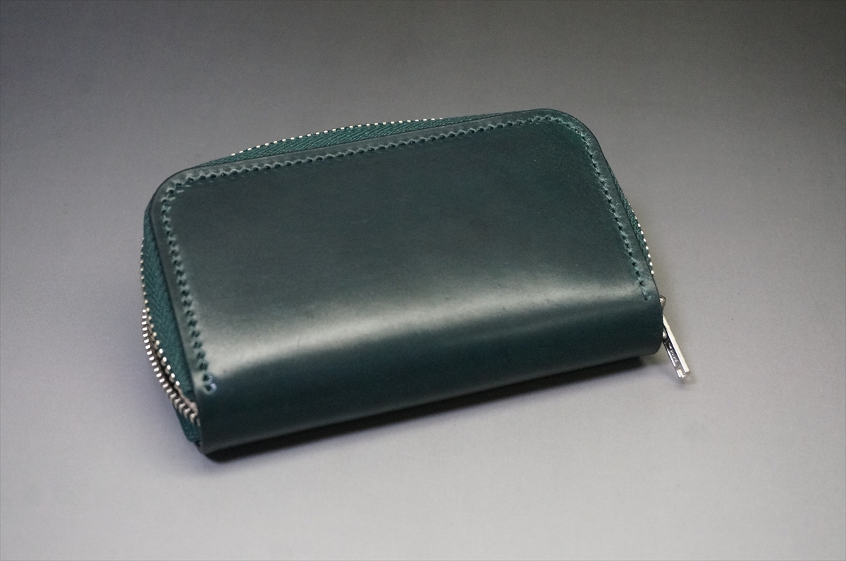 Teal leather zippered wallet closed on a gray background, photographed from a slight angle.