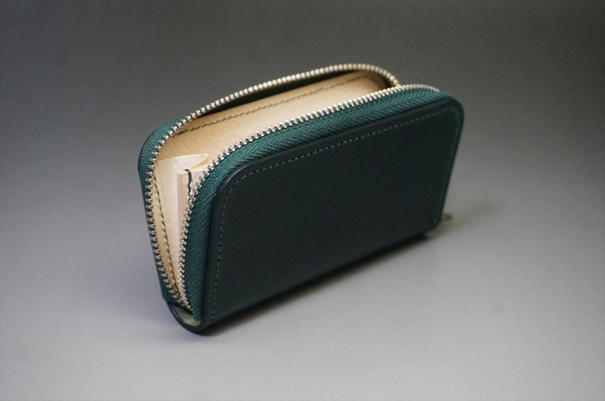 Green leather wallet with a large metal zipper, open to show a beige interior and stitched edges on a neutral background.