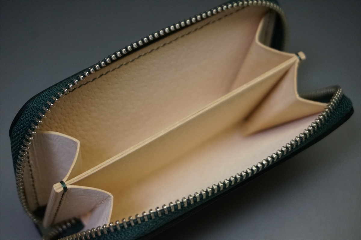 Green leather zippered wallet opened to reveal a beige suede interior and empty compartments inside.
