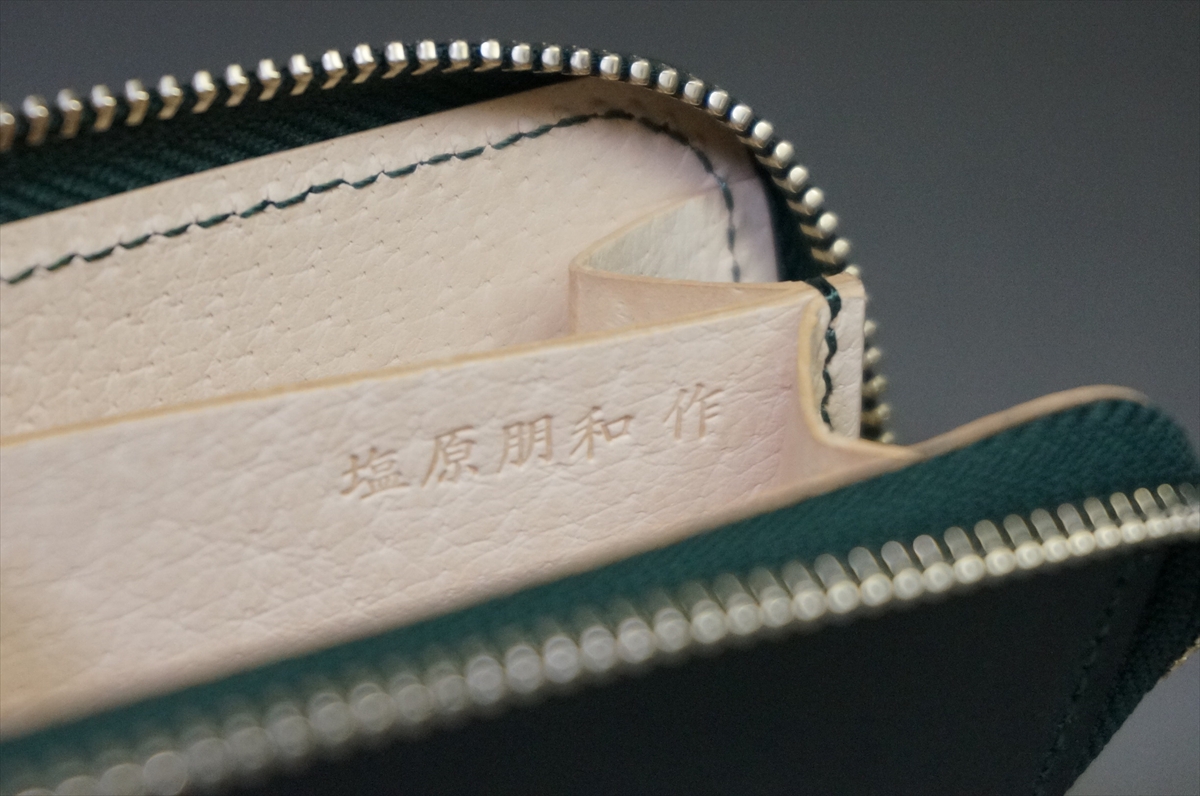 Close-up of a beige leather interior with embossed Japanese characters inside a dark green zippered wallet, showing stitching and the zipper teeth edge.