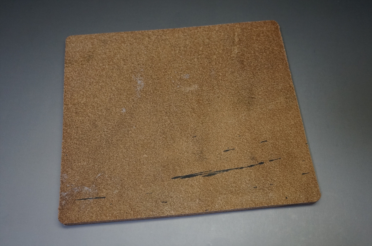 Square cork tile with rounded corners on a gray surface, showing a plain brown textured cork.