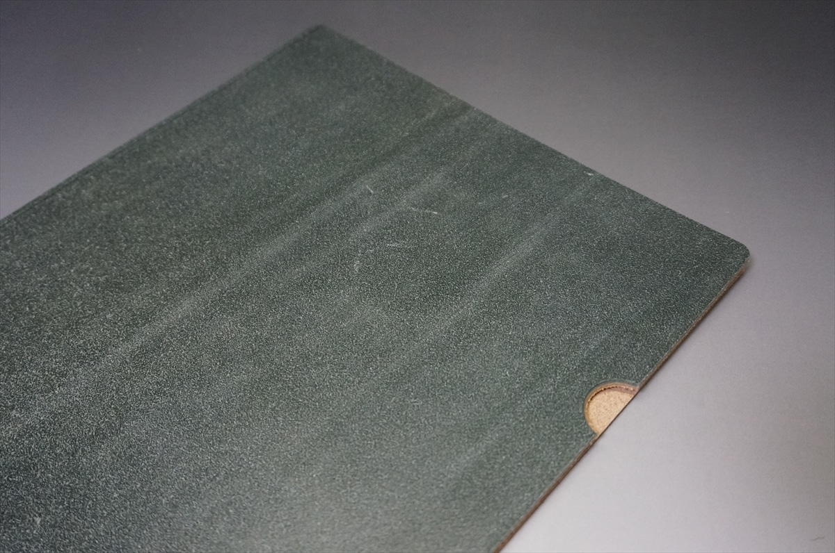 Close-up of a dark green filing folder with a beige circular tab in the bottom-right corner.