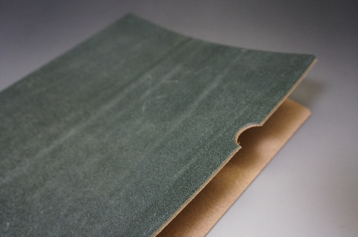 Close-up of a green textured panel with a curved notch along the edge, resting on a brown backing board.