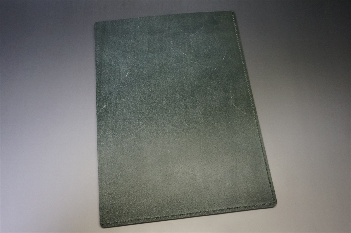 Green textured notebook with stitched edges resting on a gray surface.