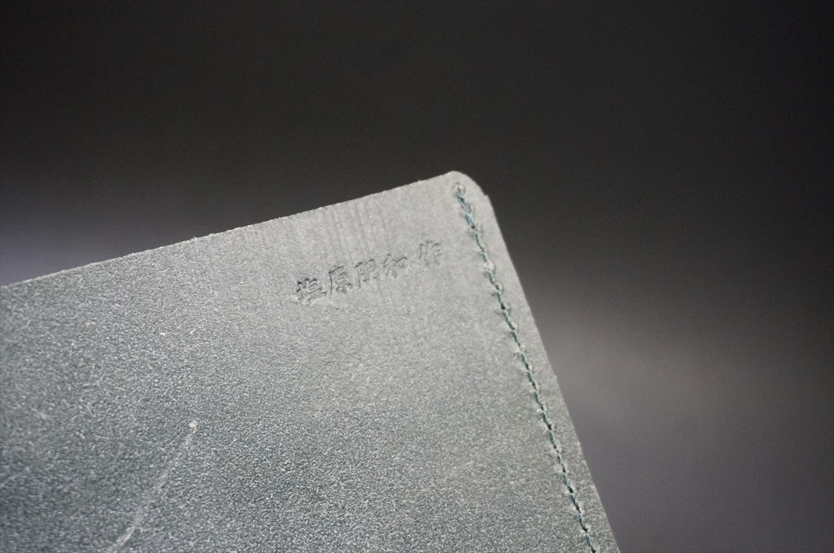 Close-up of a gray textured edge with teal stitching and small embossed Chinese characters nearby
