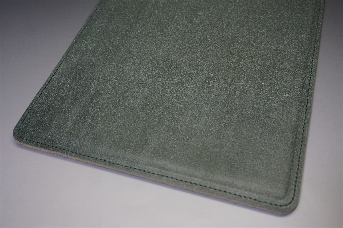 Close-up of a green suede notebook or tablet cover corner with visible stitching along the edge