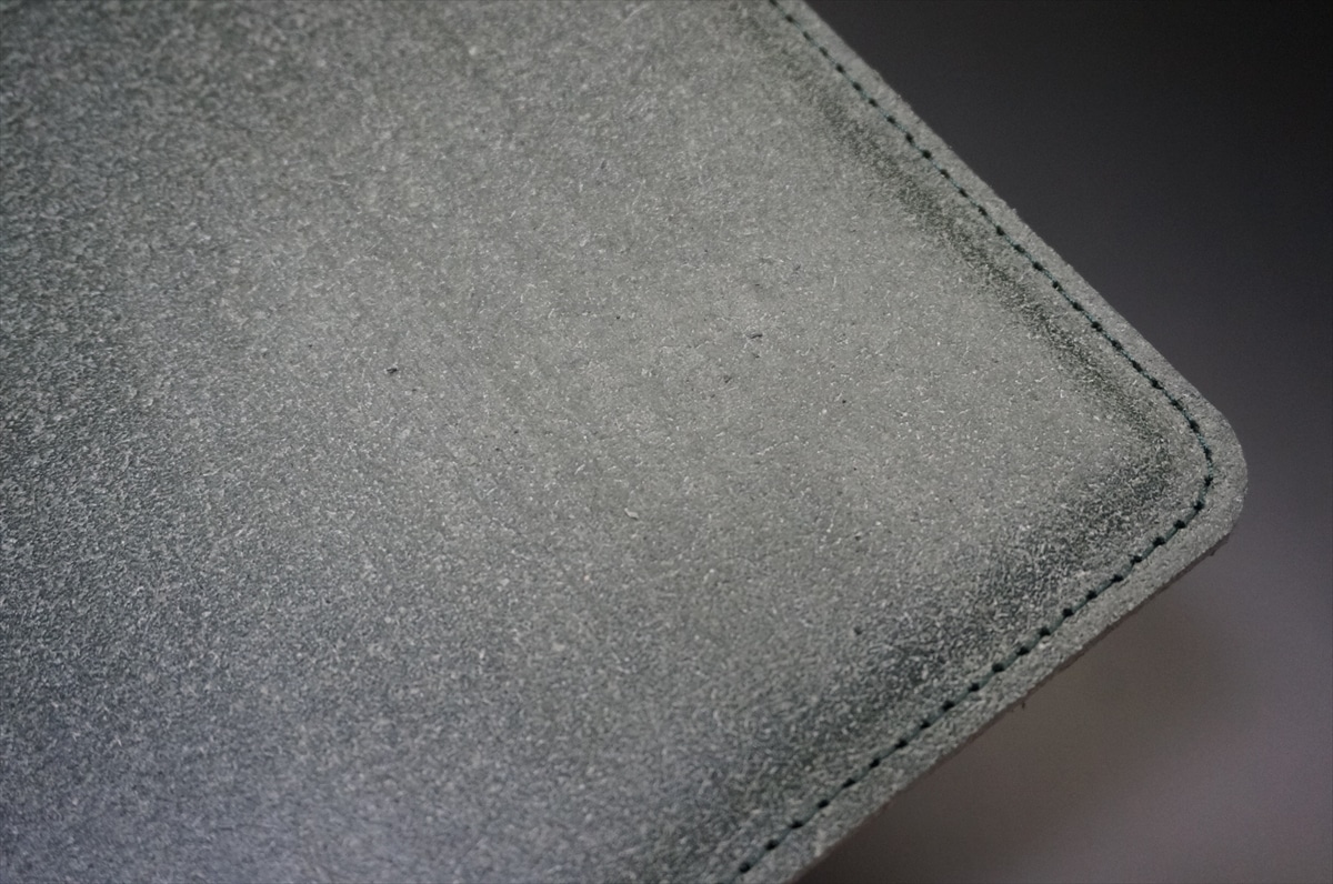 Close-up of a gray leather wallet corner with visible stitching and dusty texture