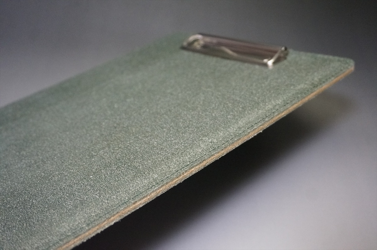 Close-up of a green abrasive sandpaper sheet with a metal clip at the top edge for fastening