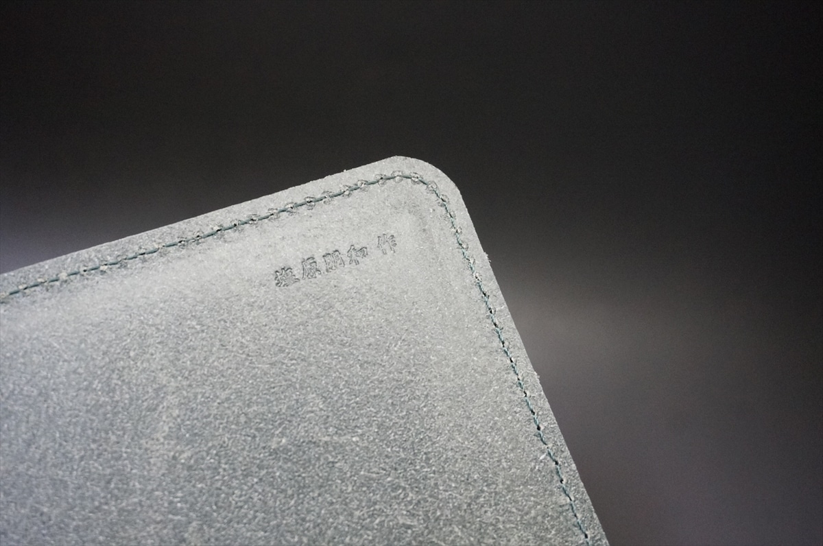 Close-up of a grey suede item with blue stitching along the edge and small embossed text in the corner.