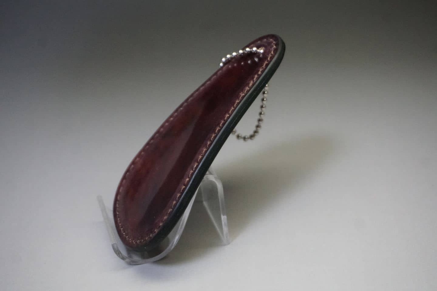 Maroon leather key fob with white stitching on a clear display stand.