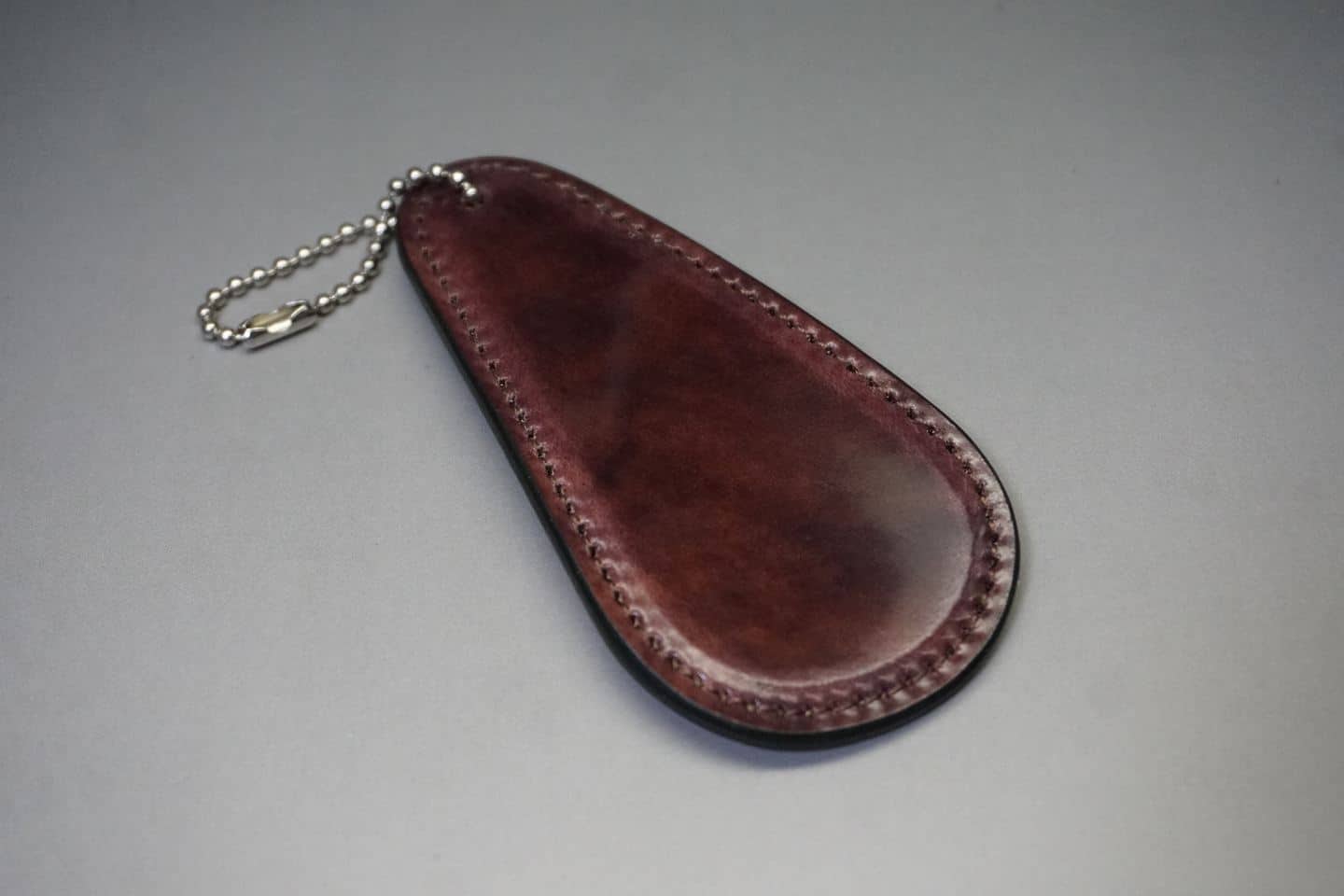 Brown teardrop-shaped leather key case with a silver ball chain attached to the top corner.